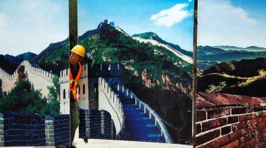 A worker looks through the fence of a construction site that is decorated with pictures of the Great Wall at Badaling, north of Beijing, China, September 1, 2016. REUTERS/Thomas Peter